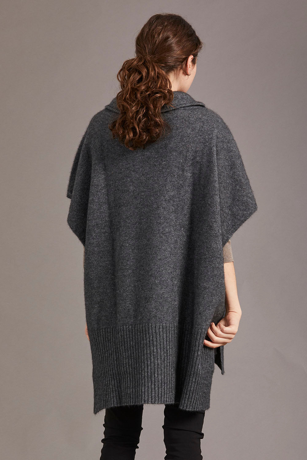 A model wearing a gray poncho with a cowl neck and a step level hem, standing against a neutral background.