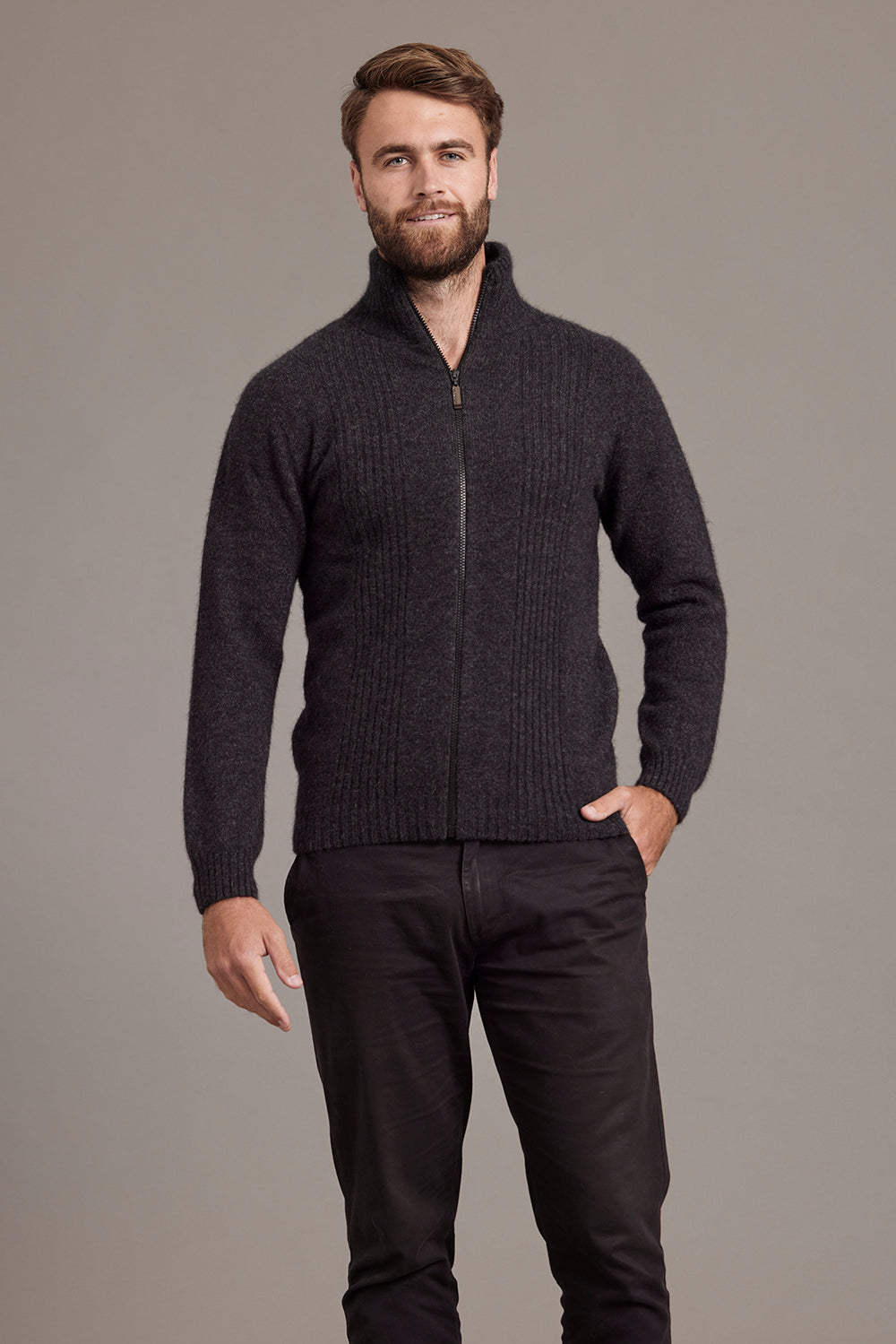 Man wearing a charcoal grey zip-up sweater against a gray background