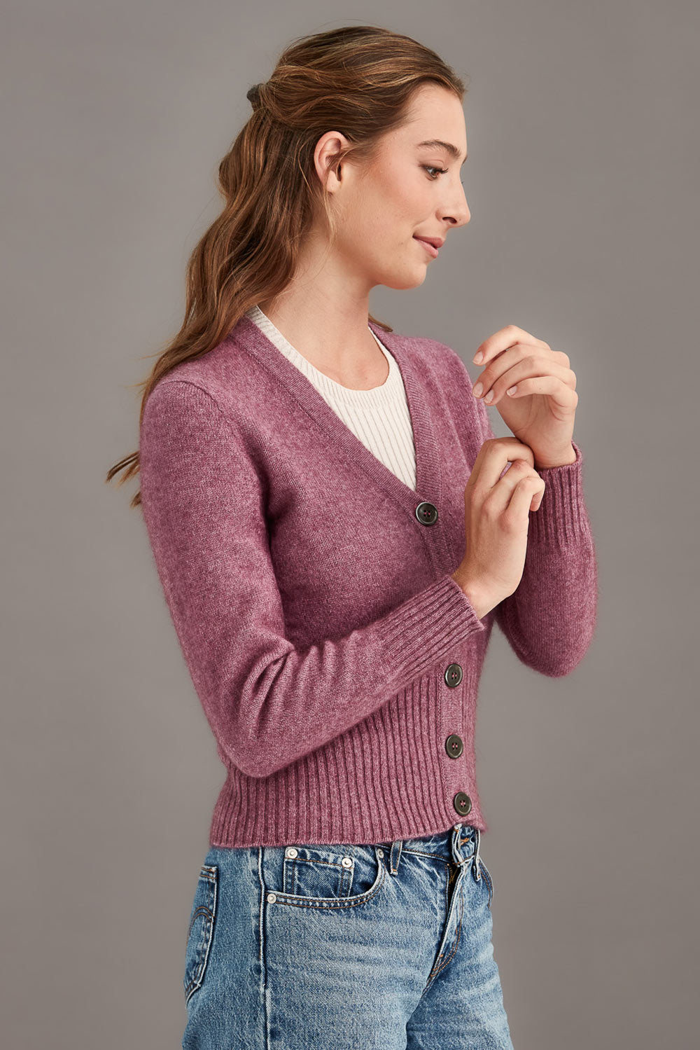 Woman wearing a pink cardigan with black buttons on a gray background