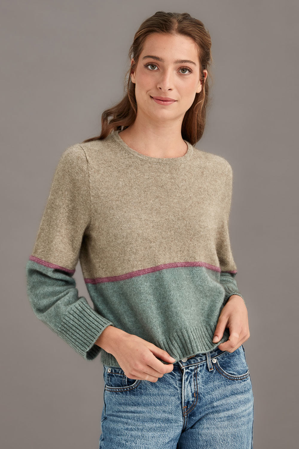 Woman wearing a colourblocked sweater with green and beige colors on a gray background